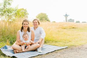 Familie sitzt auf einer Picknickdecke am Rand eines Felds, der Tower des Flughafen Bremen im Hintergrund