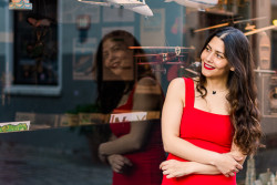 Portrait einer jungen Frau mit dunklen Haaren und rotem Kleid. Sie lehnt gegen ein Schaufenster, ihre Spiegelung ist zu sehen. Schnoor-Viertel Bremen