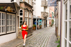 Ganzkörper-Portrait einer jungen Frau mit dunklen Haaren und rotem Kleid. Sie spaziert durch das Schnoor-Viertel Bremen